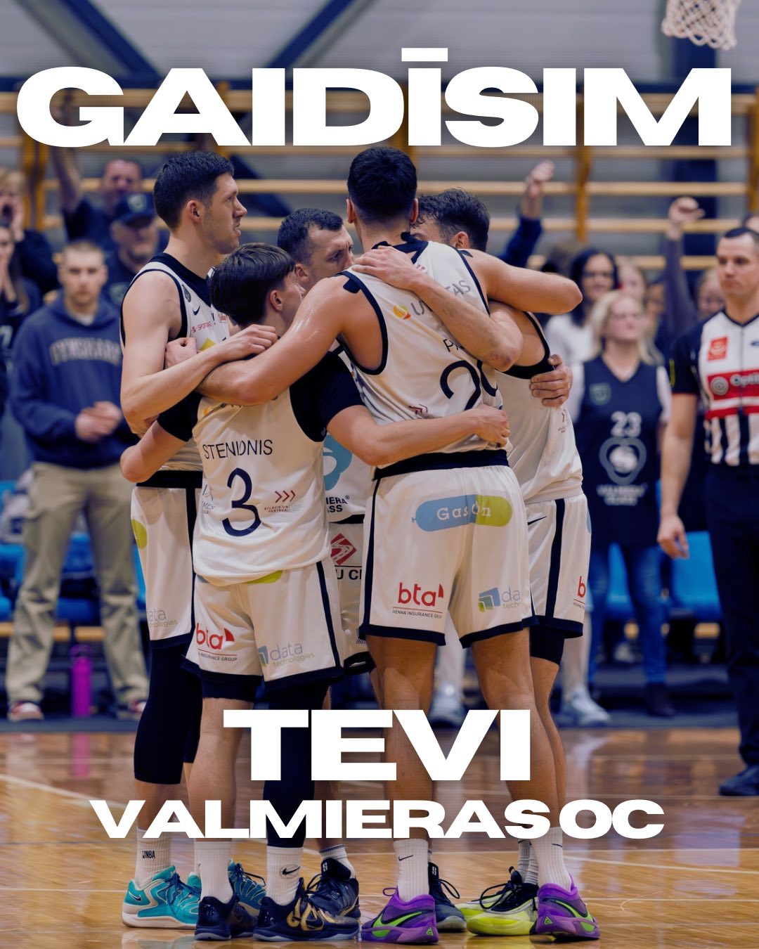 Foto ar Valmiera Glass VIA basketbola komandu, kuras spēlētāji pēc uzvaras apskāvušies laukumā Valmieras Olimpiskajā centrā. Fonā redzami līdzjutēji tribīnēs. Attēlā uzraksts: “Gaidīsim tevi Valmieras OC”, aicinot līdzjutējus apmeklēt komandas spēles.